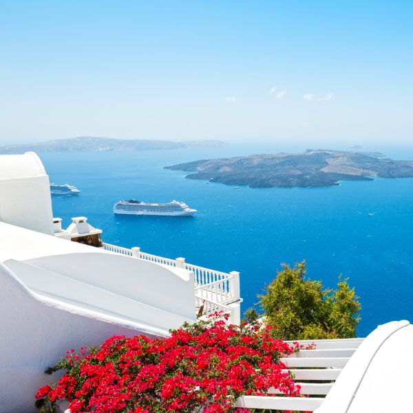 Navires de croisière ancrés dans les eaux bleues de la caldeira de Santorin, vus depuis une colline aux maisons blanchies à la chaux et aux bougainvilliers colorés