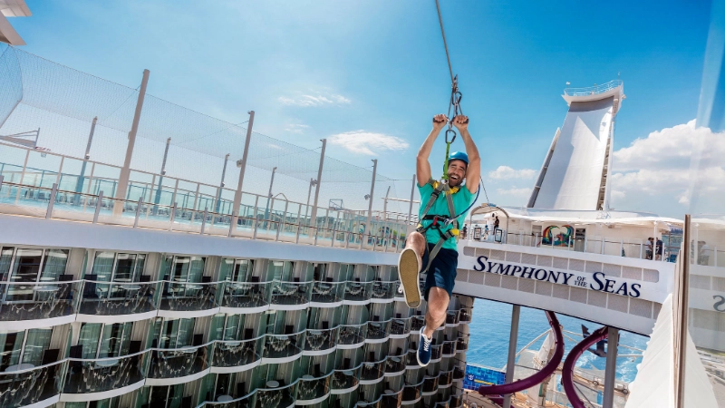 Guest riding a zip line above the deck of Royal Caribbean's Symphony of the Seas cruise ship