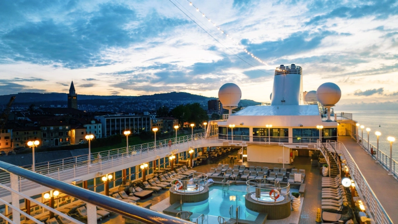 azamara cruise ship pool deck illuminated at sunset while docked beside a coastal city